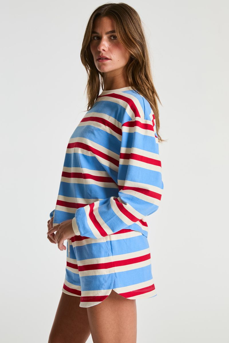 A woman modeling a long-sleeve striped lounge set featuring a blue, red, and cream horizontal stripe pattern, photographed against a solid light gray background.