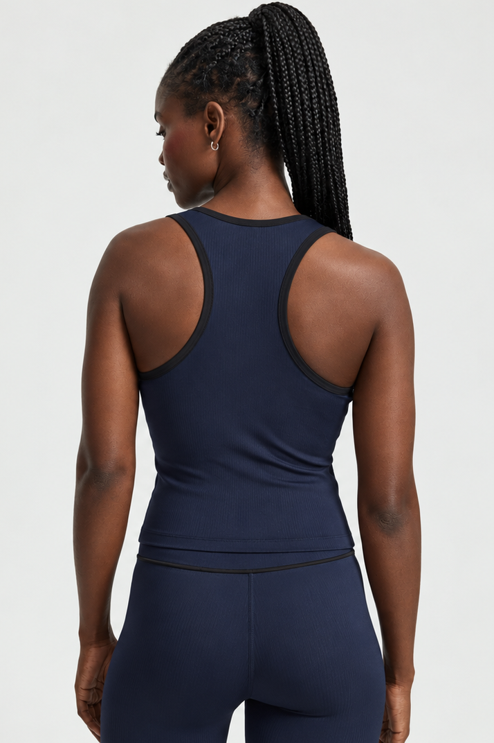 Rear view of a woman with braided hair wearing a navy ribbed athletic tank top and matching leggings with black trim, against a light gray studio background.