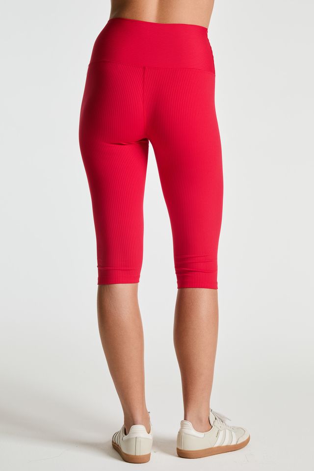 A person shown from the back wearing bright red ribbed capri leggings and white sneakers against a clean light gray studio background.