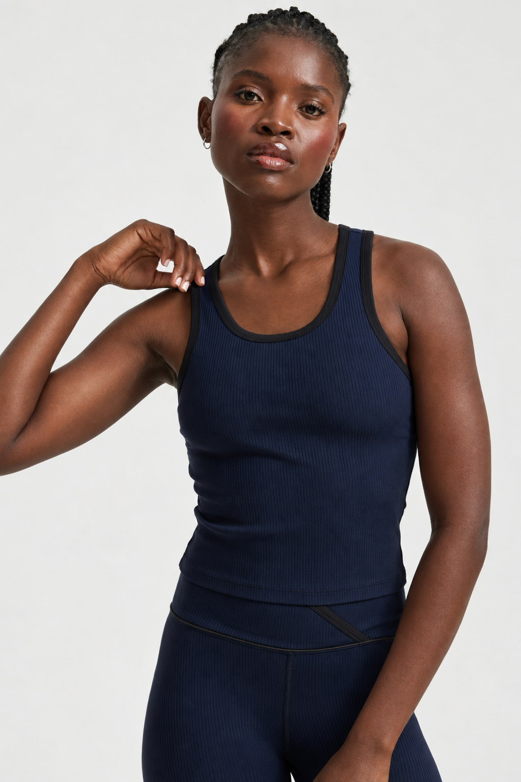 A woman modeling a dark navy ribbed tank top and matching leggings with black trim, photographed against a clean light gray studio background.